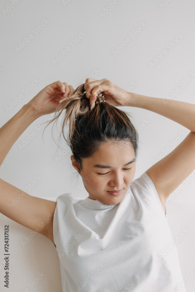 Fototapeta premium Asian woman in white t-shirt tying her hair to refresh and getting ready for the day.