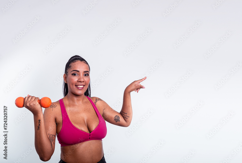 Beautiful woman dressed in gym clothes holding dumbbells and pointing finger to the side. Beautiful woman dressed in gym clothes holding dumbbells and pointing finger to the side.