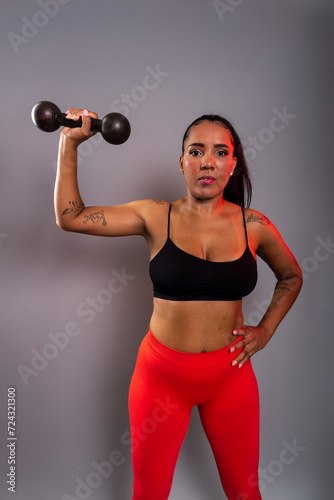 Fototapeta Naklejka Na Ścianę i Meble -  Beautiful brunette woman, in gym clothes, holding black dumbbells at head height. Healthy life.