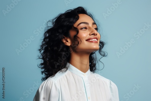 Portrait of happy young woman smiling and looking away against blue background