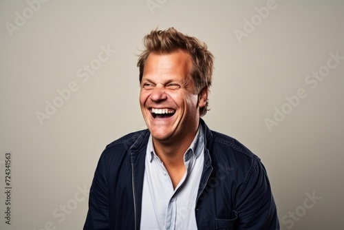 Portrait of a happy young man laughing against a grey background. © Iigo