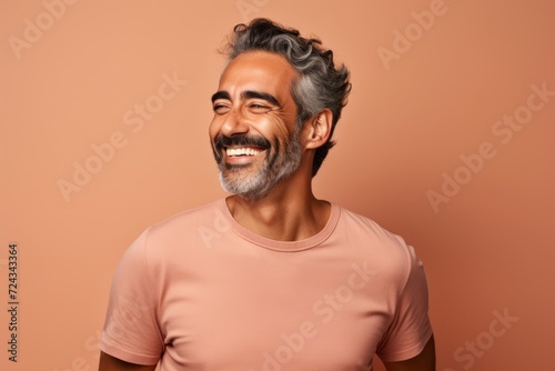 Portrait of happy mature Indian man in casual t-shirt, isolated on brown background