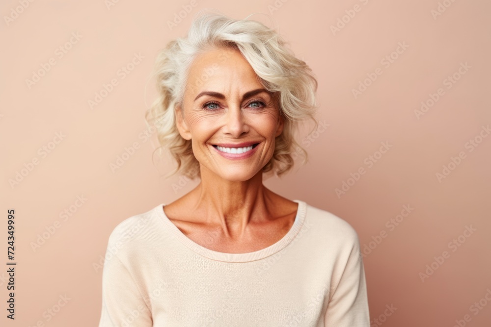 Portrait of smiling senior woman looking at camera over beige background
