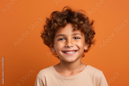 Portrait of a smiling little boy with curly hair on orange background © Iigo