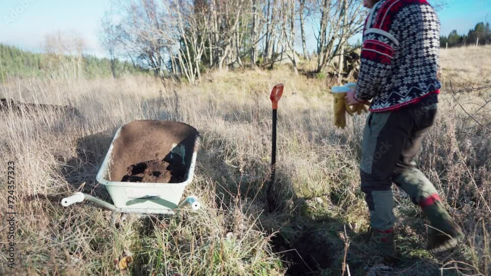 A Man Excavates Soil and Transfers it into a Wheelbarrow for the Construction of a Greenhouse - Static Shot A Man Excavates Soil and Transfers it into a Wheelbarrow for the Construction of a Greenhouse - Static Shot