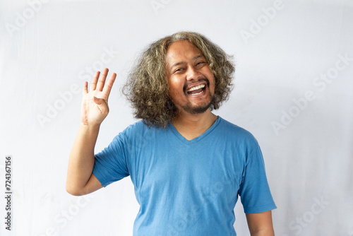 A handsome, curly-headed man wearing light blue clothes stood and laughed with his hands raised showing numbers. Photo of cheerful man isolated on white background.