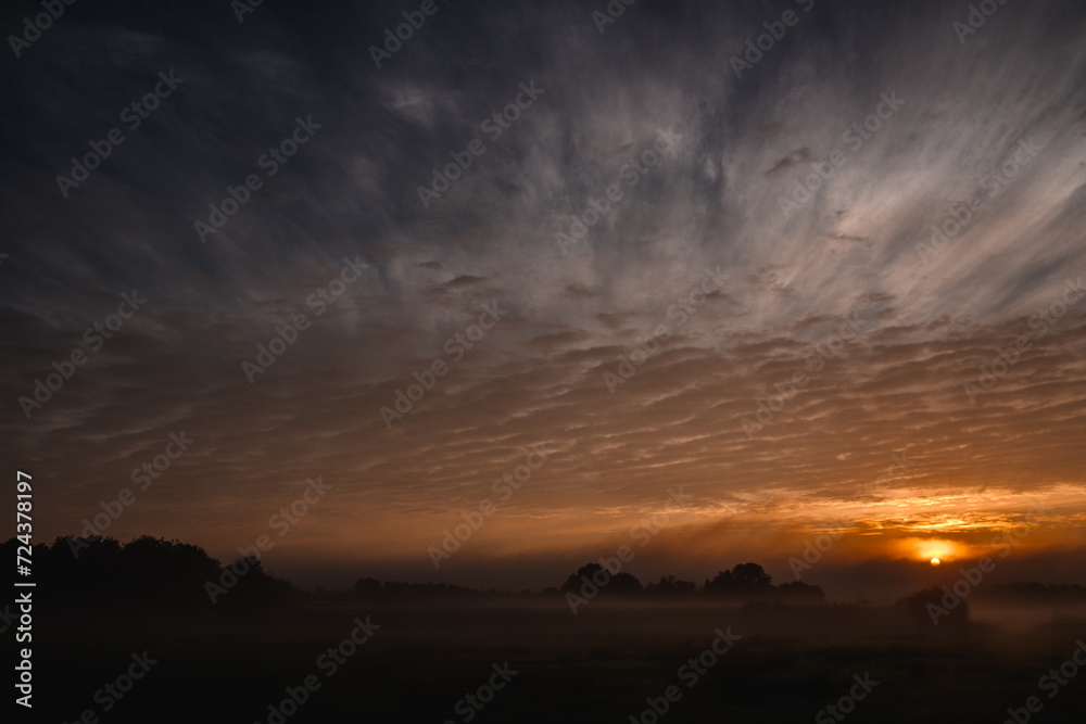 This compelling image showcases the intense and brooding beauty of twilight. The dark, expansive sky is streaked with dramatic cloud formations, while the setting sun provides a fiery focal point