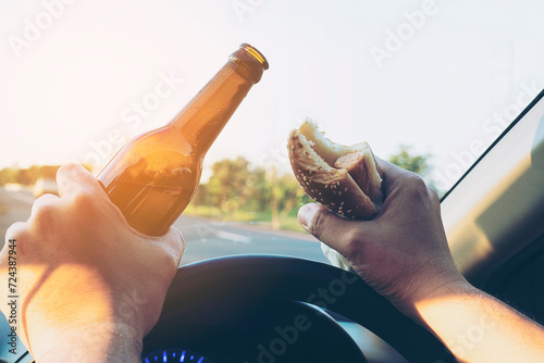 Man eating hotdog with beer while driving a car dangerously photo