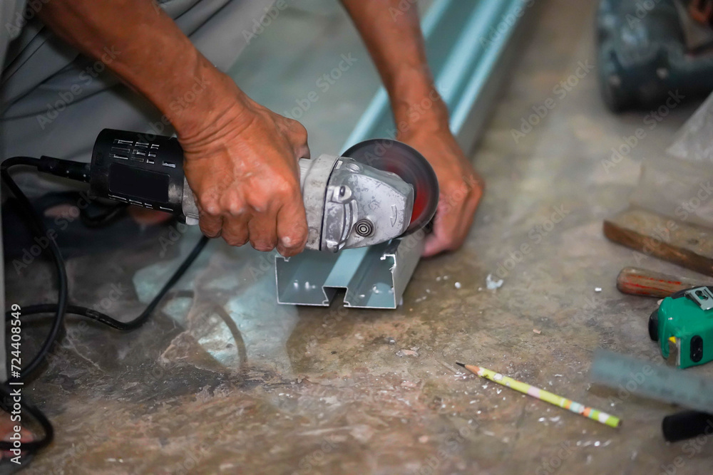 Closeup hands of the master saw the metal holding electric angle grinder working in construction site.