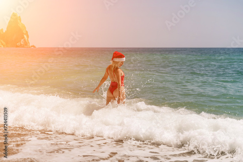 A woman in Santa hat on the seashore, dressed in a red swimsuit. New Year's celebration in a hot country © svetograph