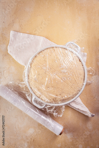 Yeast dough covered by plastic wrap, proofed dough for baking bread or pizza