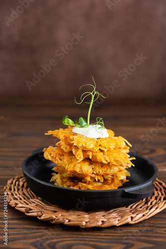 Crispy potato pancakes, draniki, Latkes or Levivot with sour cream and green on a stacked cast iron frying pan. Hanukkah food. During the Jewish Festival of Lights holiday. Vertical orientation. photo