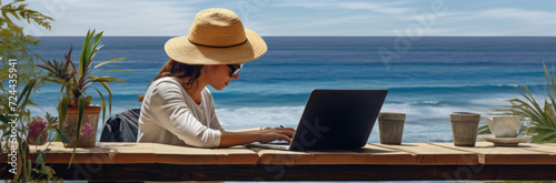 Rear view of young woman, female freelancer in straw hat working on laptop, while sitting on the tropical sandy beach © Ruslan Gilmanshin