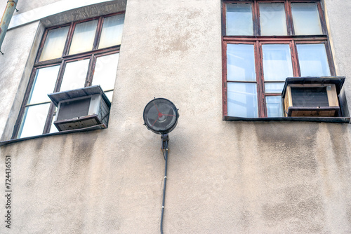 Gray old wall with a lantern in the middle and two windows, view from below.