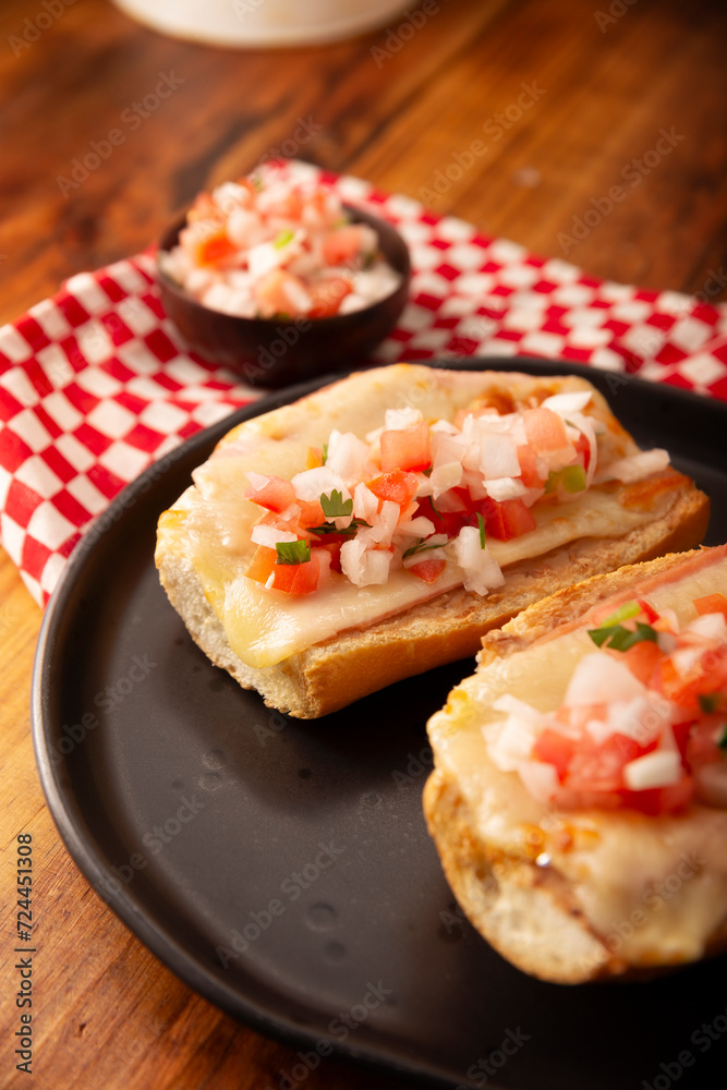 Molletes. Mexican recipe based on bolillo bread split lengthwise, spread with refried beans and gratin cheese, adding pico de gallo sauce and some protein such as ham, bacon or chorizo.