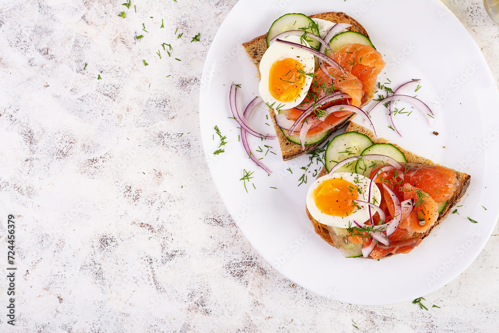 Delicious toast with salmon, boiled egg, cucumber and cream cheese on a white plate. Healthy eating, breakfast. Keto diet food. Tasty food. Top view