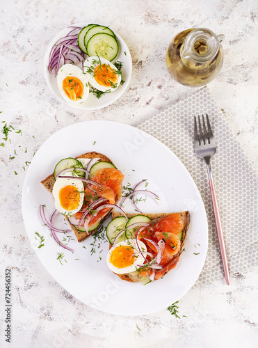 Delicious toast with salmon, boiled egg, cucumber and cream cheese on a white plate. Healthy eating, breakfast. Keto diet food. Tasty food. Top view