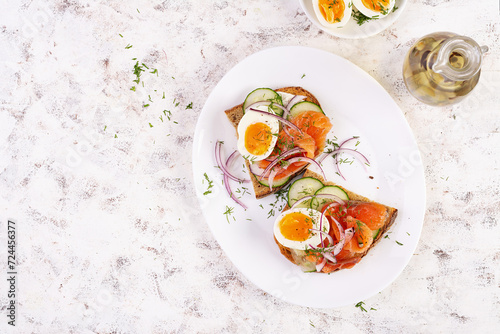 Delicious toast with salmon, boiled egg, cucumber and cream cheese on a white plate. Healthy eating, breakfast. Keto diet food. Tasty food. Top view