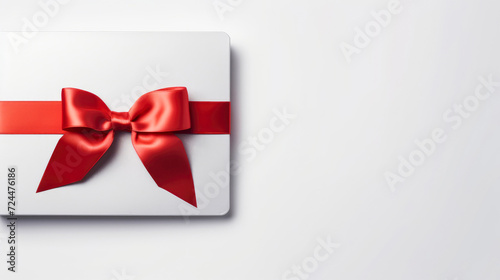 Blank white gift card with a red ribbon bow on a grey background with minimal shadow and conceptual design. Copy space.