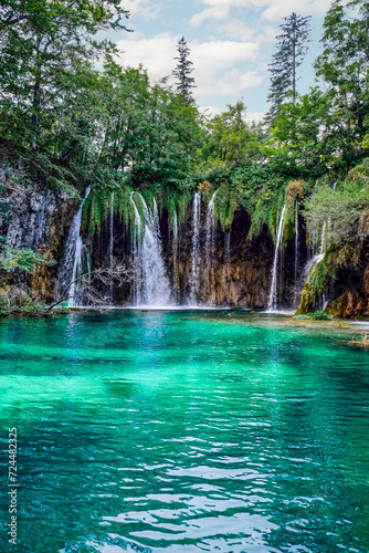 Fototapeta Naklejka Na Ścianę i Meble -  Low angle view of multiple waterfalls streaming into a beautiful, tranquil, clear lake at Plitvice Lakes National Park