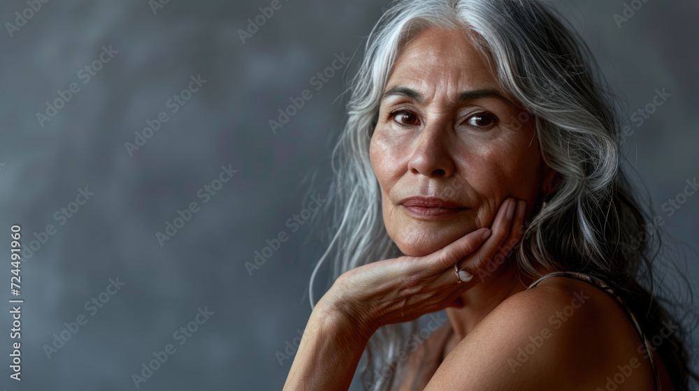 Mature woman with long silver hair poses thoughtfully with her hand on her cheek Mature woman with long silver hair poses thoughtfully with her hand on her cheek