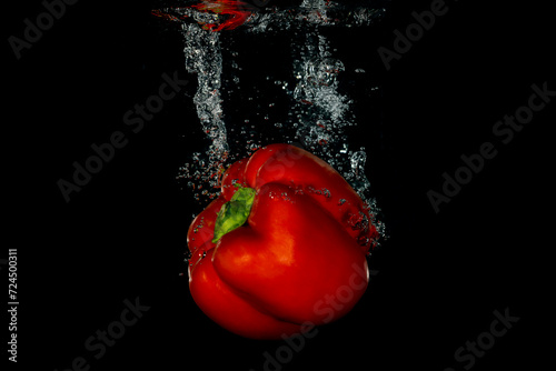 Whole red bell pepper falling into water with a black background creating bubbles