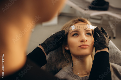 The master checks the contour of the eyebrows of the client before the procedure with a special ruler. Permanent Eyebrow Makeup Procedure. High quality photo