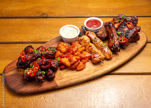 Assorted meats: chicken nuggets, pork ribs, Buffalo chicken wings, chicken kebab, sauce, on a wooden board photo