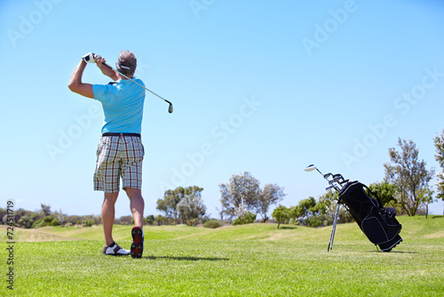 Senior, man and playing golf on field, lawn or green grass for sports, swing or taking a shot on course. Rear view of person, golfer or player hitting ball, strike or goal to score point in nature