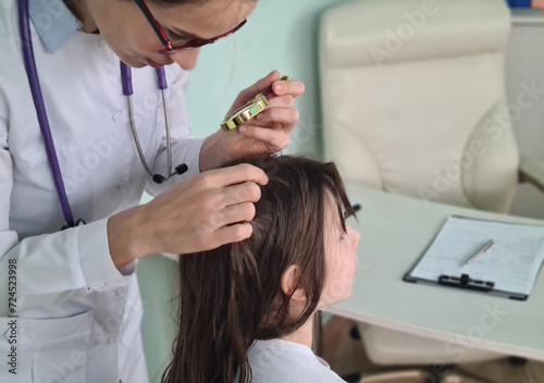 Female doctor examining childs scalp for lice or nits with a magnifying glass in a medical clinic