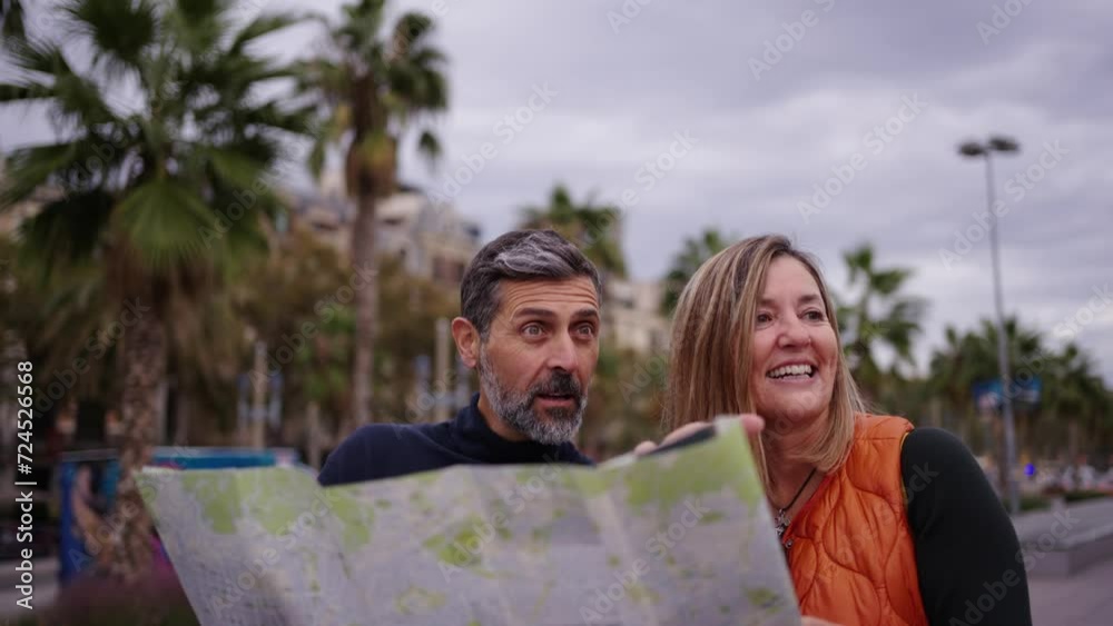 Middle-aged Caucasian couple speaking holding travel map looking and pointing places of tourist interest. Husband and wife on street of city enjoying vacation happy and laughing. Adult tourism people Middle-aged Caucasian couple speaking holding travel map looking and pointing places of tourist interest. Husband and wife on street of city enjoying vacation happy and laughing. Adult tourism people