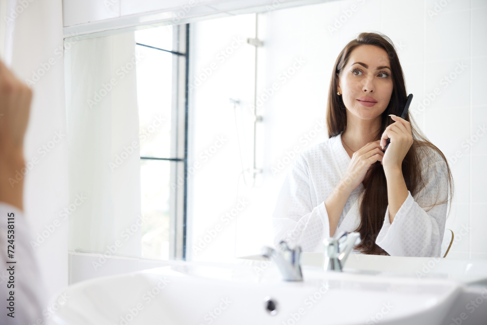 young woman combing hair in front of mirror at bathroom young woman combing hair in front of mirror at bathroom