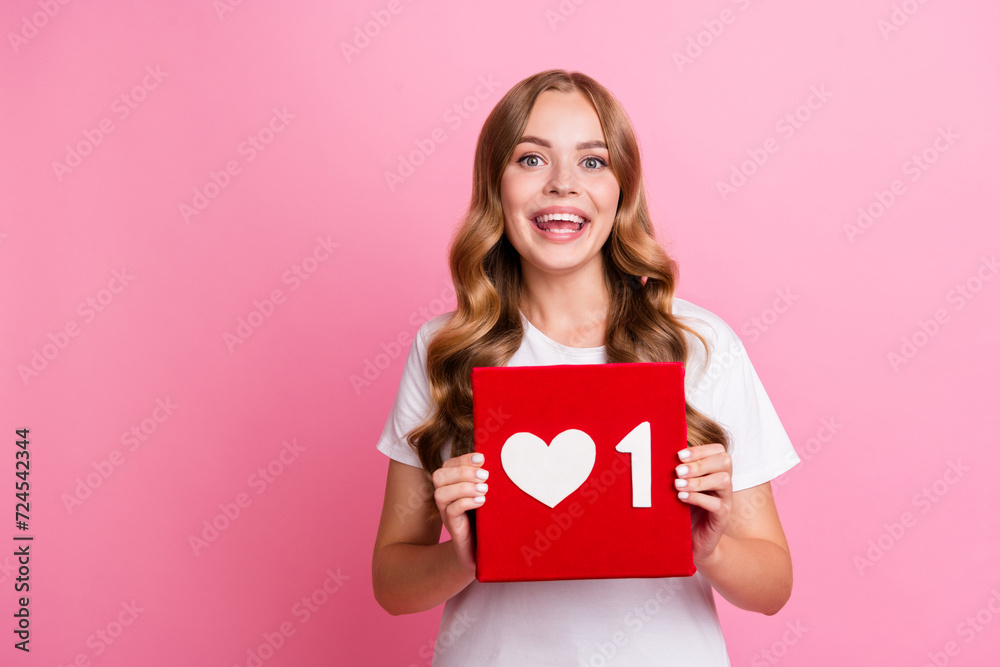 Portrait of young smiling very optimistic blogging girl in white t shirt holding red like symbol repost isolated on pink color background Portrait of young smiling very optimistic blogging girl in white t shirt holding red like symbol repost isolated on pink color background