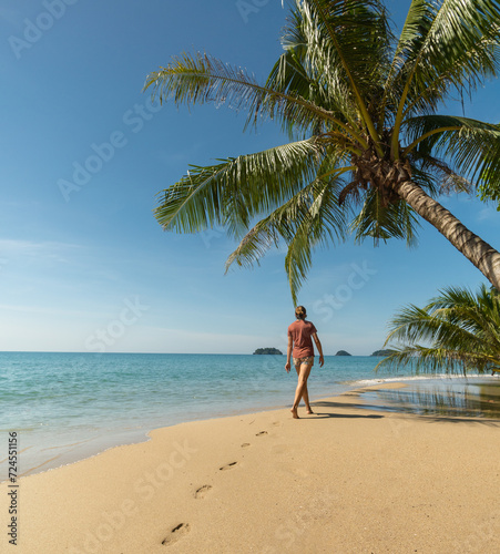 woman walks on tropical sandy beach under palm trees