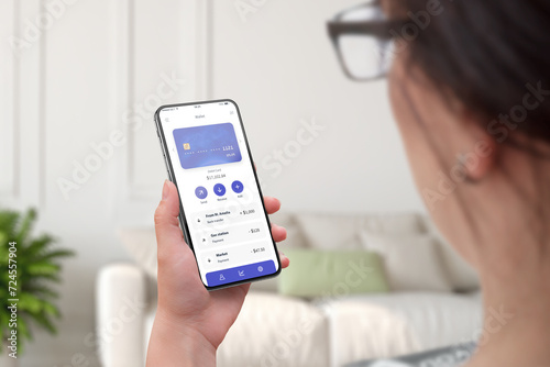 Woman's hands hold a phone with a fintech app, featuring a modern card, account selector, and a list of transactions. Facilitating financial technology management with user-friendly interfaces