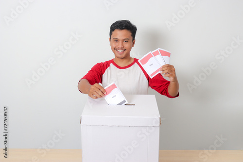 Portrait of excited Asian man inserting and putting the voting paper into the ballot box. General elections or Pemilu for the president and government of Indonesia. Isolated image on white background