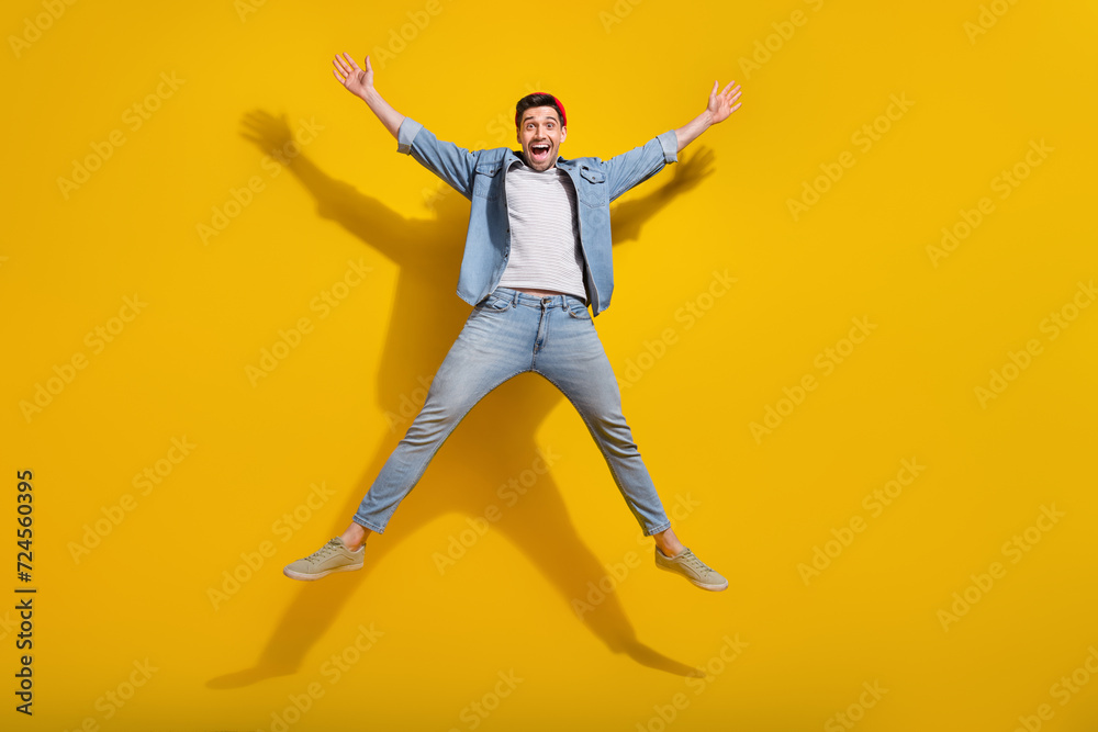 Full length photo of excited good mood guy wear denim jacket jumping high like star isolated yellow color background