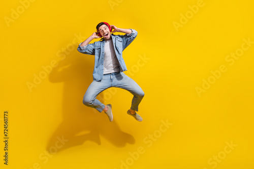 Full length photo of funky impressed guy wear denim jacket jumping high enjoying songs empty space isolated yellow color background © deagreez