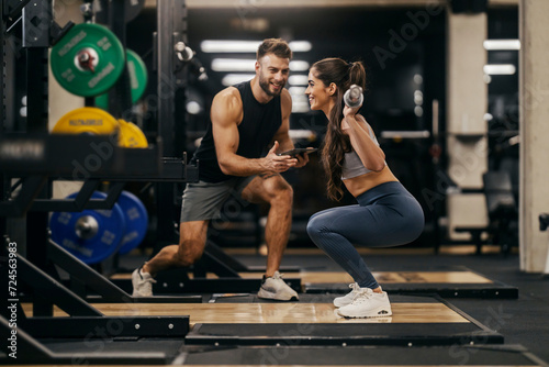 Foto Side view of a sportswoman lifting bar in a gym with personal trainer support
