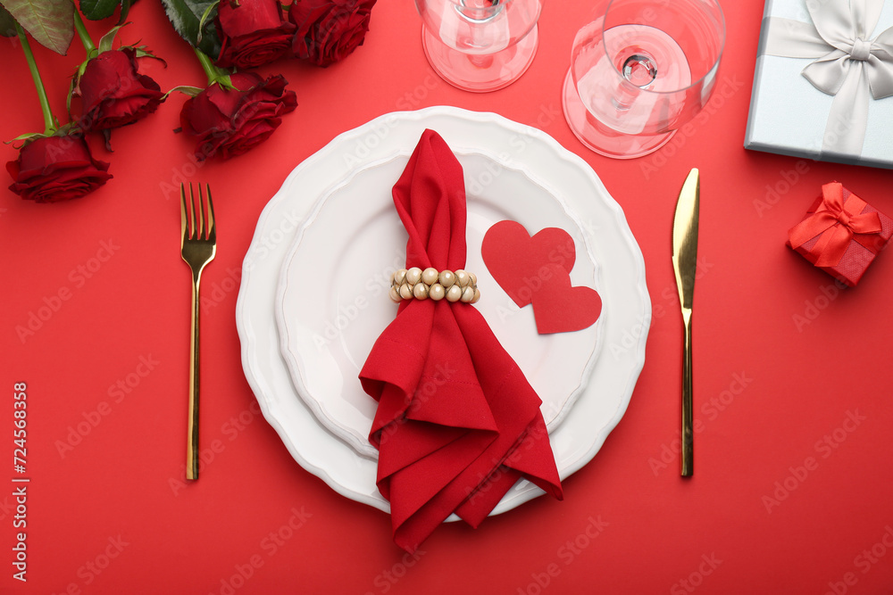 Place setting with paper hearts, gift boxes and bouquet of roses on red table, flat lay. Romantic dinner Place setting with paper hearts, gift boxes and bouquet of roses on red table, flat lay. Romantic dinner