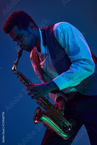 African-American man virtuoso, solo musician playing jazz melodies on saxophone against gradient blue background in mixed neon light. Concept of jazz, blues, classy instrumental music, concert. Ad photo