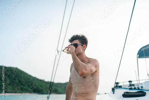 Caucasian man hand holding champagne glass relax and enjoy luxury outdoor lifestyle while travel on catamaran boat yacht sailing in the ocean at sunset on summer beach holiday vacation trip