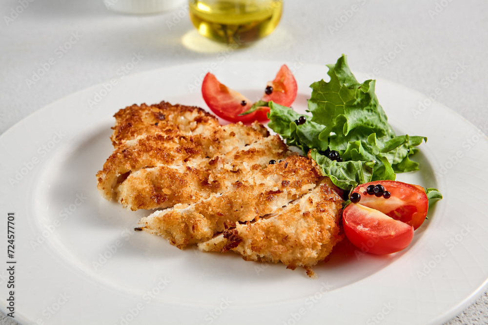 Golden crusted chicken fillet with cheese on a bed of lettuce, topped with cherry tomatoes, ideal for recipes and menu designs
