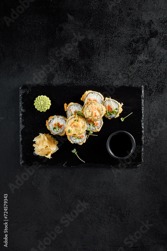 Salmon tempura roll top view on a textured black slate with condiments