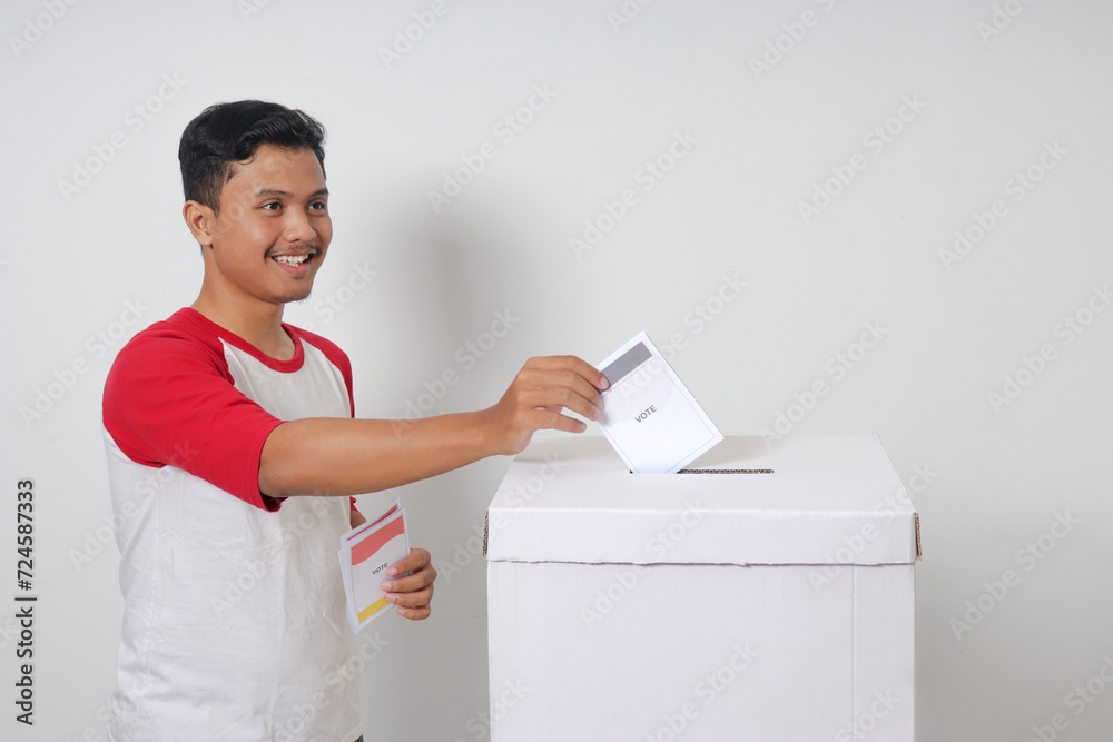 Portrait of excited Asian man inserting and putting the voting paper into the ballot box. General elections or Pemilu for the president and government of Indonesia. Isolated image on white background Portrait of excited Asian man inserting and putting the voting paper into the ballot box. General elections or Pemilu for the president and government of Indonesia. Isolated image on white background