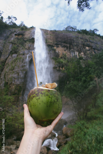 hand holding a king coconut against the backdrop of a waterfall  photo