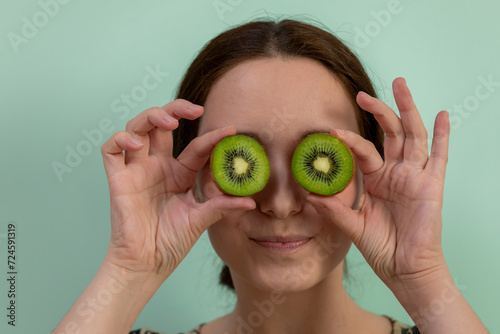 Portrait of a young woman holding halves of kiwi over her eyes. 