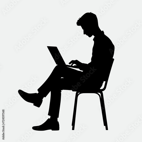 A silhouette of a man working on a laptop while sitting on a chair