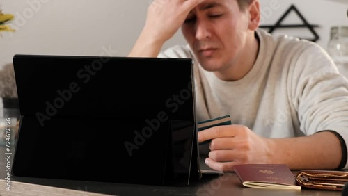 Disappointed man looking at his laptop with credit card in hand