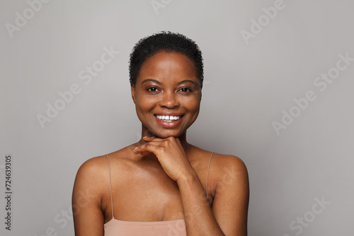 Smiling African American female model with healthy fresh clear dark skin posing on white background. Skin care, cosmetology and beauty treatment